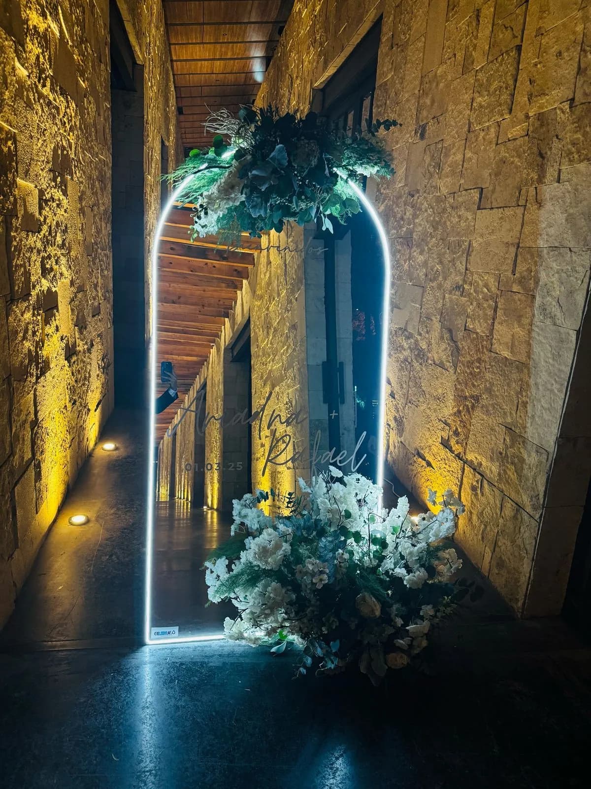 Espejo arqueado con luz LED y flores en un pasillo de piedra