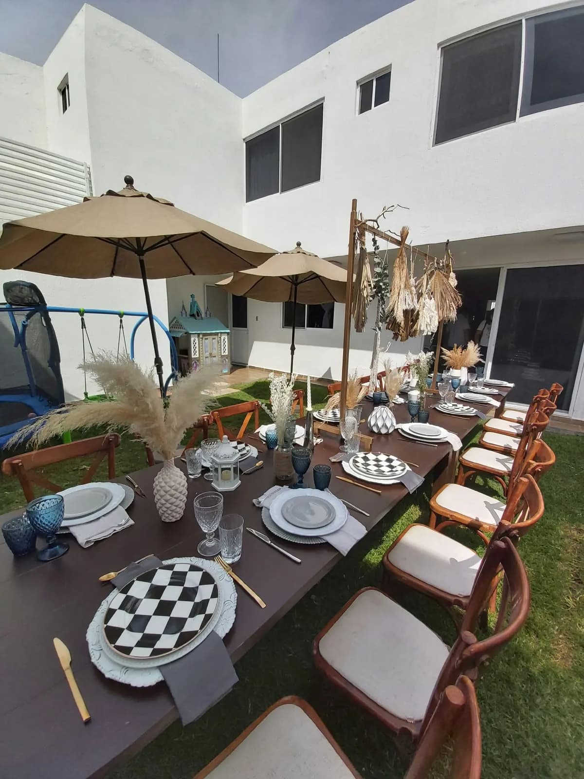 Mesa larga en un jardín con platos a cuadros y pampas